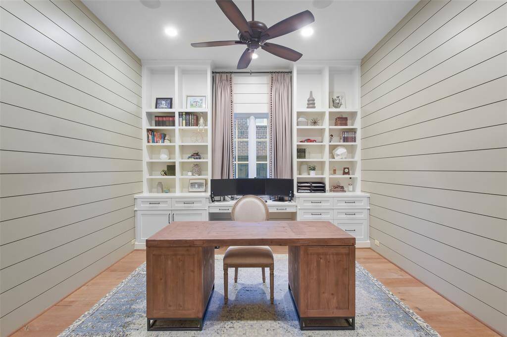 The home office offers classic shiplap paneling, a wall of built-in bookshelves that provides ample space to display books, personal treasures, and decorative accents and a large window that invites natural light to pour in.