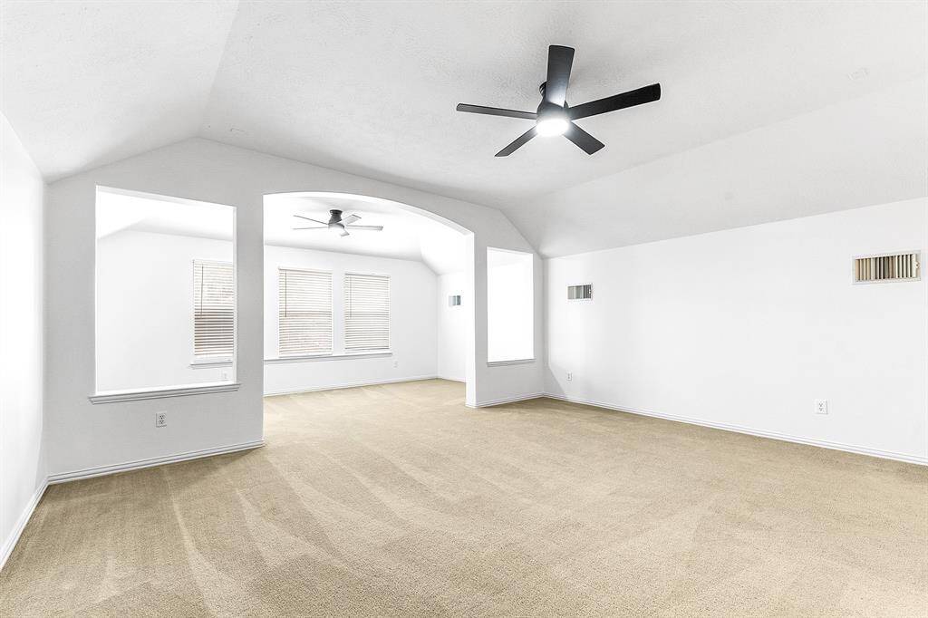 Another view of this upstairs bonus space reveals dual ceiling fans controlled by two separate remotes, allowing for comfortable airflow in distinct areas. The room is thoughtfully designed to create two separate spaces, offering beautiful backyard views.