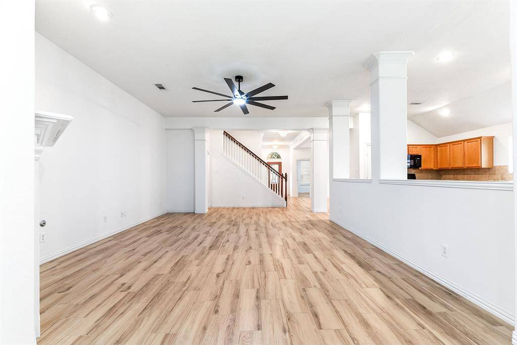 This home features an open-concept layout with a spacious living room showcasing wood-like tile floors and high ceilings. A drop-down ceiling fan with remote adds comfort and style, while recessed lighting highlights the cozy gas fireplace.