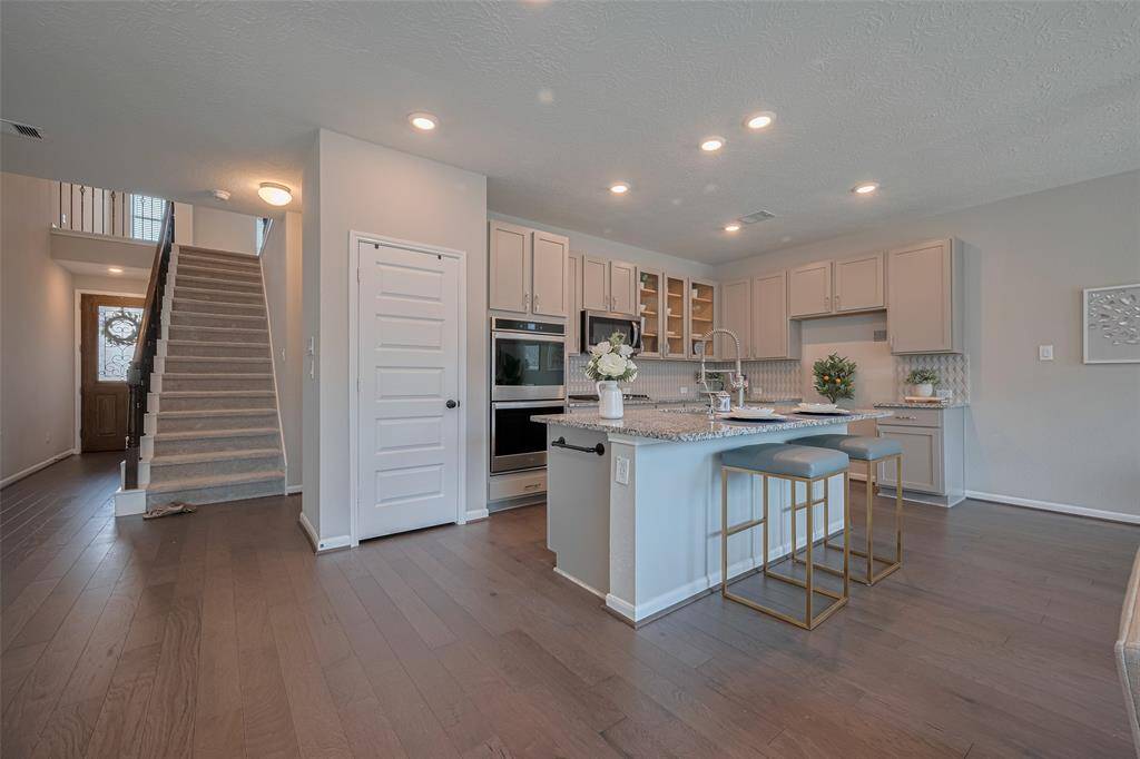 Kitchen featuring tall closet, two ovens, stainless appliances, granite countertops, glass cabinet and more.