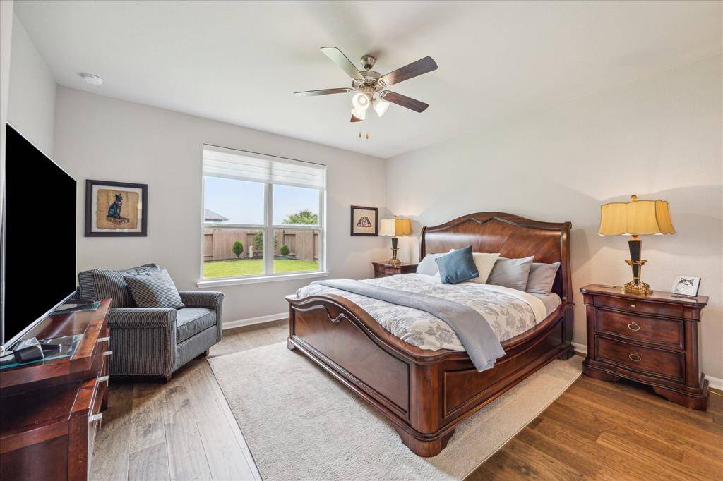 The primary suite is located at the rear of the home and boasts the same gorgeous wood floors as seen in the rest of the house. The custom fabric window shade can be opened partially with slats that can be raised, lowered, or angled to adjust to your light preferences, leaving a nice view of the manicured backyard.