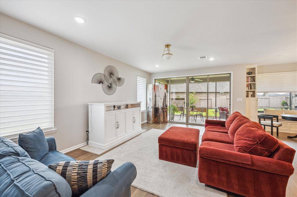 The sun-filled family room shines with natural light from two large windows and a sliding door that leads to a covered outdoor patio.  Recessed lights and a lovely ceiling light fixture help to showcase the attractive wood floors.