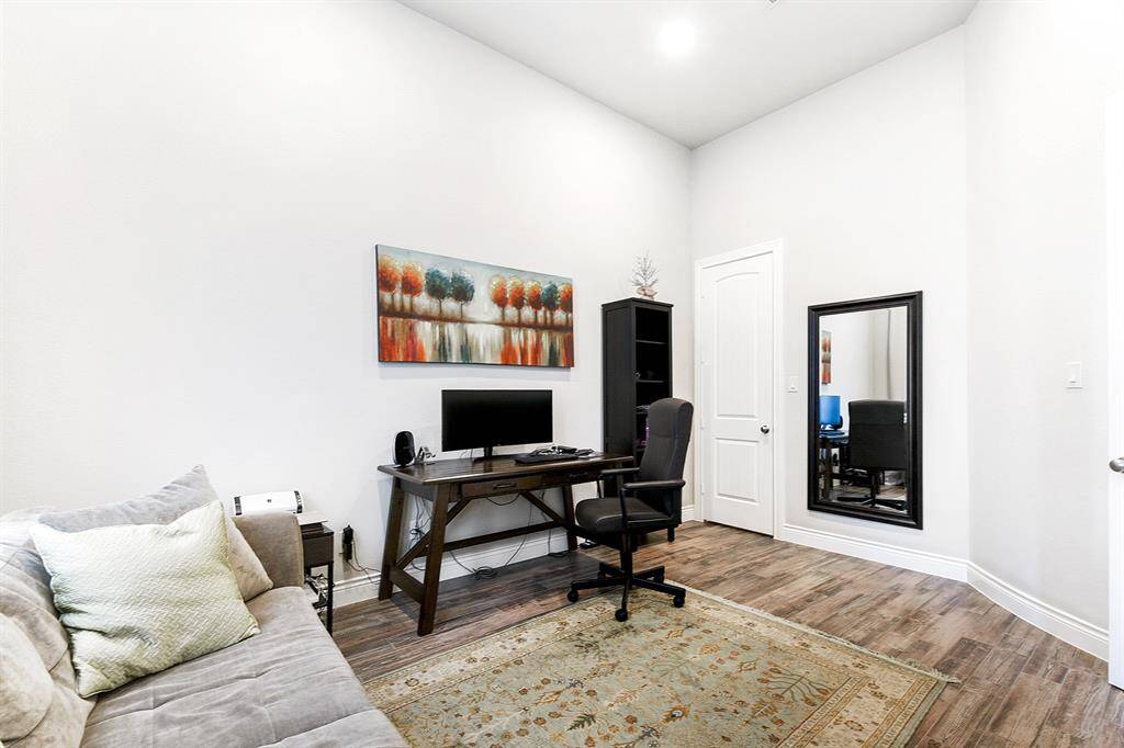 Another view of this impressive home office showcases a wall of large windows overlooking the front yard, recessed lighting, and the same wood-like tile that runs throughout the home. Notice the space this office offers, featuring both a comfortable seating area and a dedicated work space.