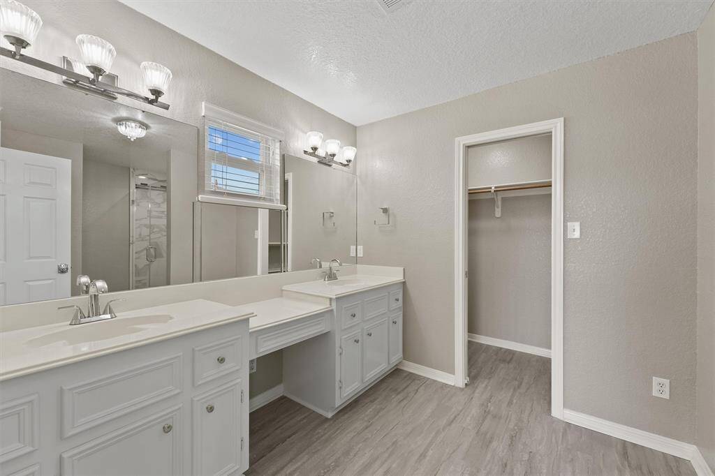 Bright and airy bath featuring dual vanities, updated lighting, and a large walk-in closet for added storage.
