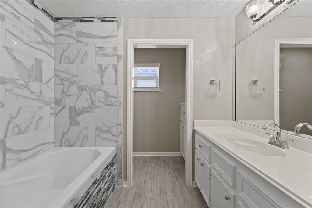 Gorgeous bathroom with double vanity, marble-look tile, and a deep soaking tub framed by custom stone accents.