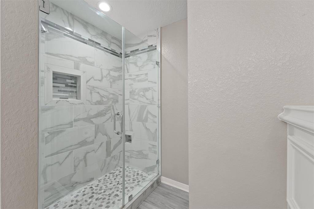Stylish walk-in shower with glass enclosure, pebble flooring, and dramatic marble-style wall tile.