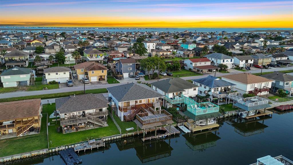 Breathtaking sunset aerial showcasing the home’s prime location in Bayou Vista with expansive views of the canals, nearby bay, and vibrant neighborhood.