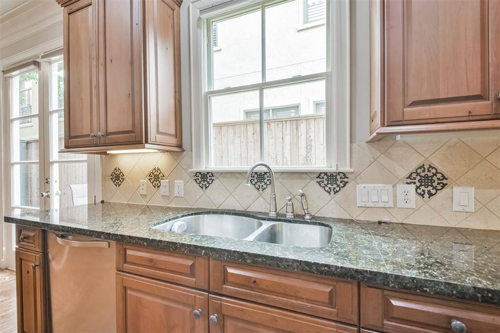 Deep double-basin stainlesssteel sink under a bright window,framed by detailed tilebacksplash and granite counters—functional and stylish.
