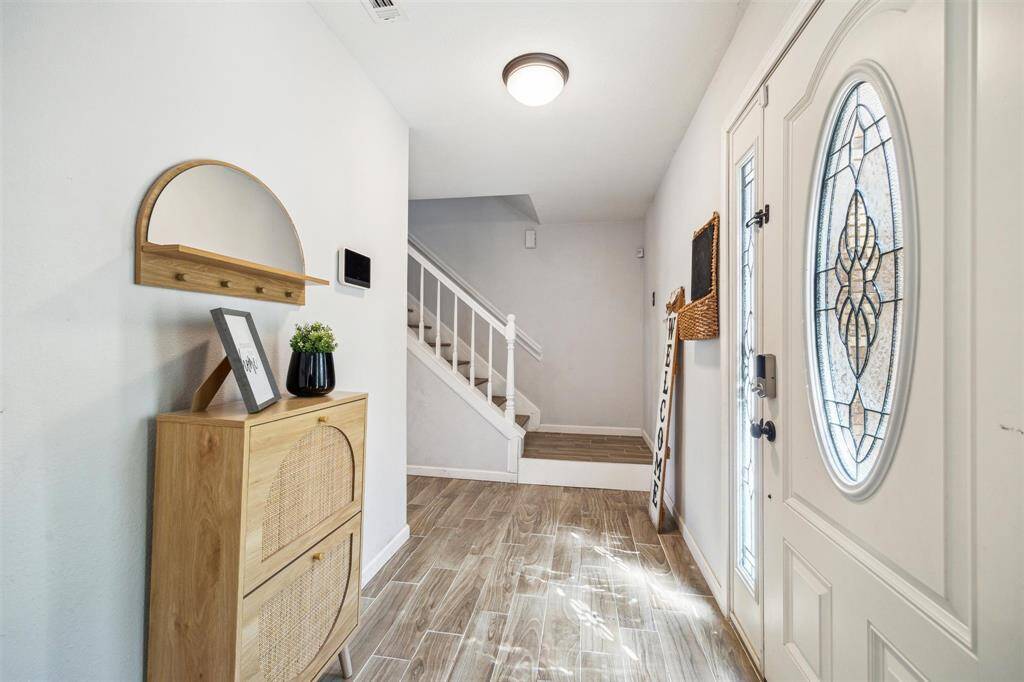 Bright and welcoming entryway featuring a decorative glass front door, wood-look tile flooring, and a stylish staircase leading to the upper level.