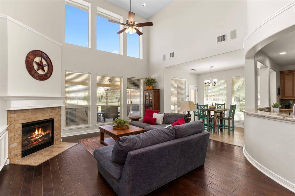 The Family Room features stunning wood floors, a soaring 18-foot ceiling, and a gas log fireplace with a 2x4 brick pattern travertine surround. A wall of windows floods the space with natural light while offering picturesque views of the backyard.