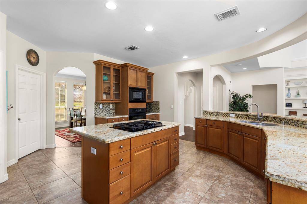 The Kitchen boasts durable 18x18 tile floors and sleek GE Profile appliance package, including a built-in microwave, oven, 4 burner gas cooktop and dishwasher. Plenty of cabinetry, accented with elegant glass-front cabinets, provides both storage and a beautiful way to display your favorite dishes.  The door to the left leads to the spacious laundry room, featuring a convenient sink, ample storage, and enough space for an extra refrigerator, making household tasks more efficient and organized.
