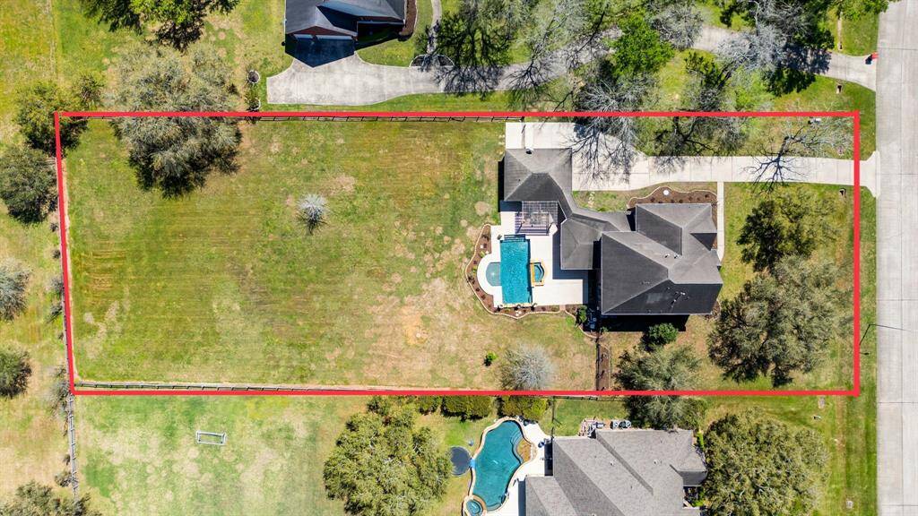 A bird’s-eye view reveals the thoughtfully designed layout, highlighting the expansive backyard, sparkling pool and spa, lush landscaping, and the full scope of the property. Approximate property lines are outlined in red for reference.
