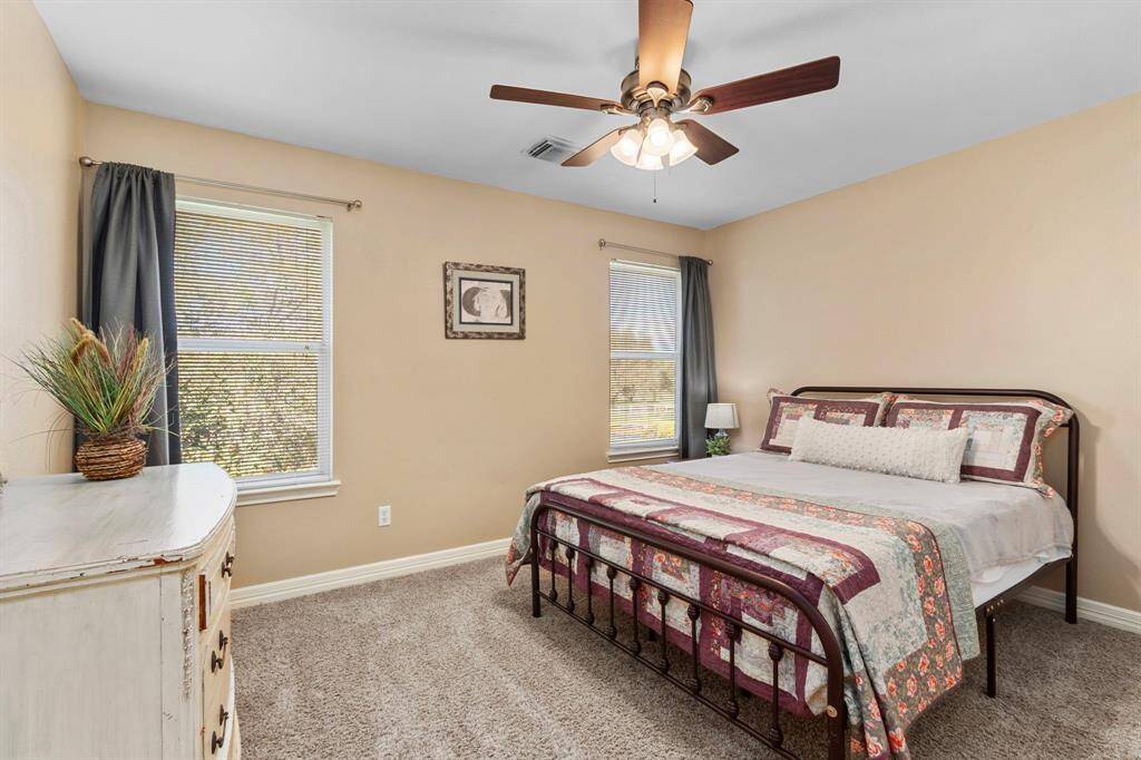 This Bedroom features soft, inviting wall colors, two large windows adorned with decorative window treatment, and an elegant oil-rubbed bronze ceiling fan, creating a warm and comfortable atmosphere.