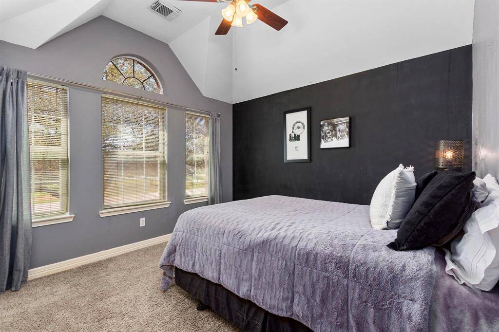 This Bedroom overlooks the front yard, featuring a stunning wall of windows with an eye-lit arched window above, allowing natural light to flood the space. The high vaulted ceiling adds to the room’s airy and spacious feel, creating a bright and inviting retreat.