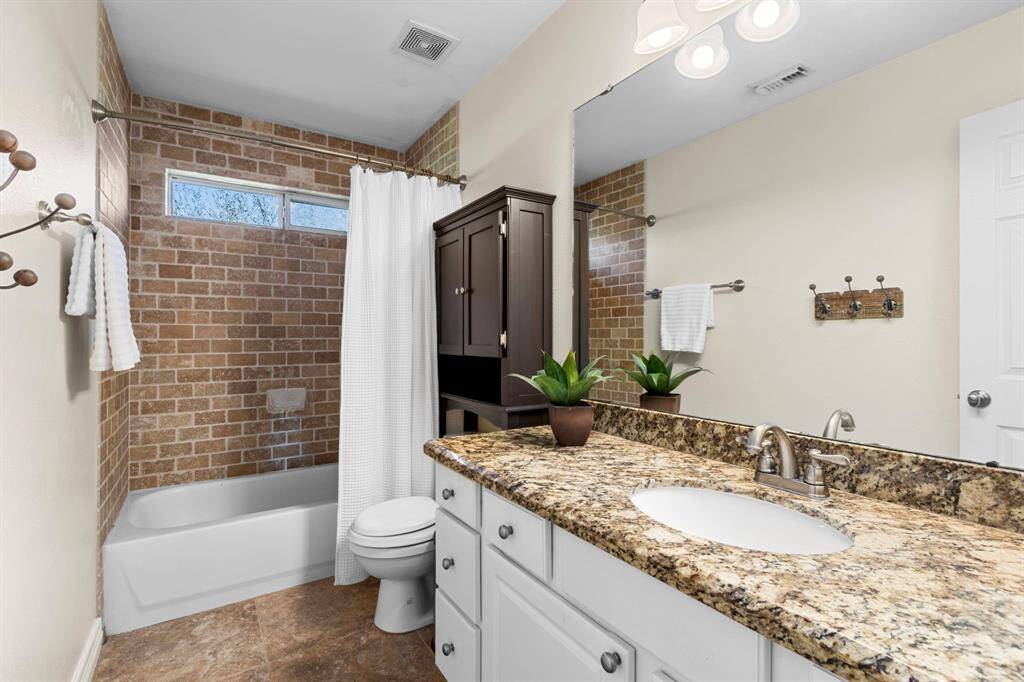This Full Bath serves the upstairs Bedrooms and features granite countertops with an undermount sink, a tub/shower combination with a 2x4 brick pattern travertine surround, and two small windows above that provide natural light. Brushed nickel faucets and light fixtures enhance the space with a stylish and modern touch.