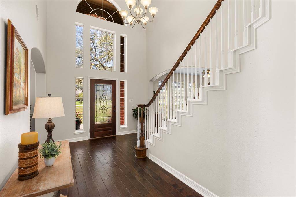 Looking back toward the Foyer, the leaded glass front door is beautifully framed by expansive windows, crowned by a striking arched window above. A radiant 7-globe chandelier enhances the space, adding elegance and warmth to the grand entrance.