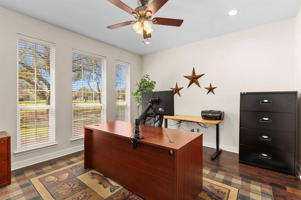 The Home Office, just off the Foyer, features rich wood floors, an oil-rubbed bronze ceiling fan, and a trio of windows that fill the space with natural light, creating an inviting and productive atmosphere.