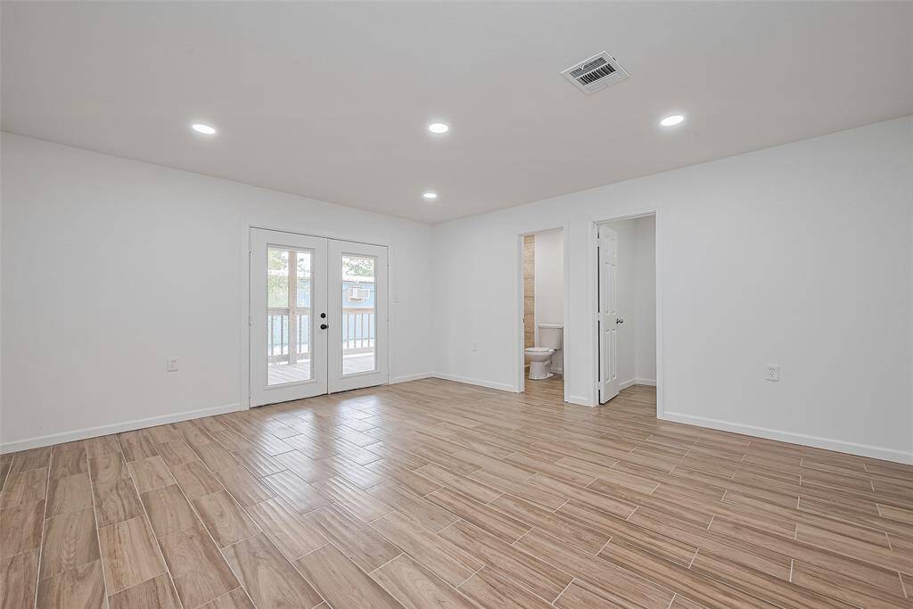 Bright and spacious room with wood-look tile flooring, recessed lighting, and multiple access points—ideal as a bedroom or flexible living space.