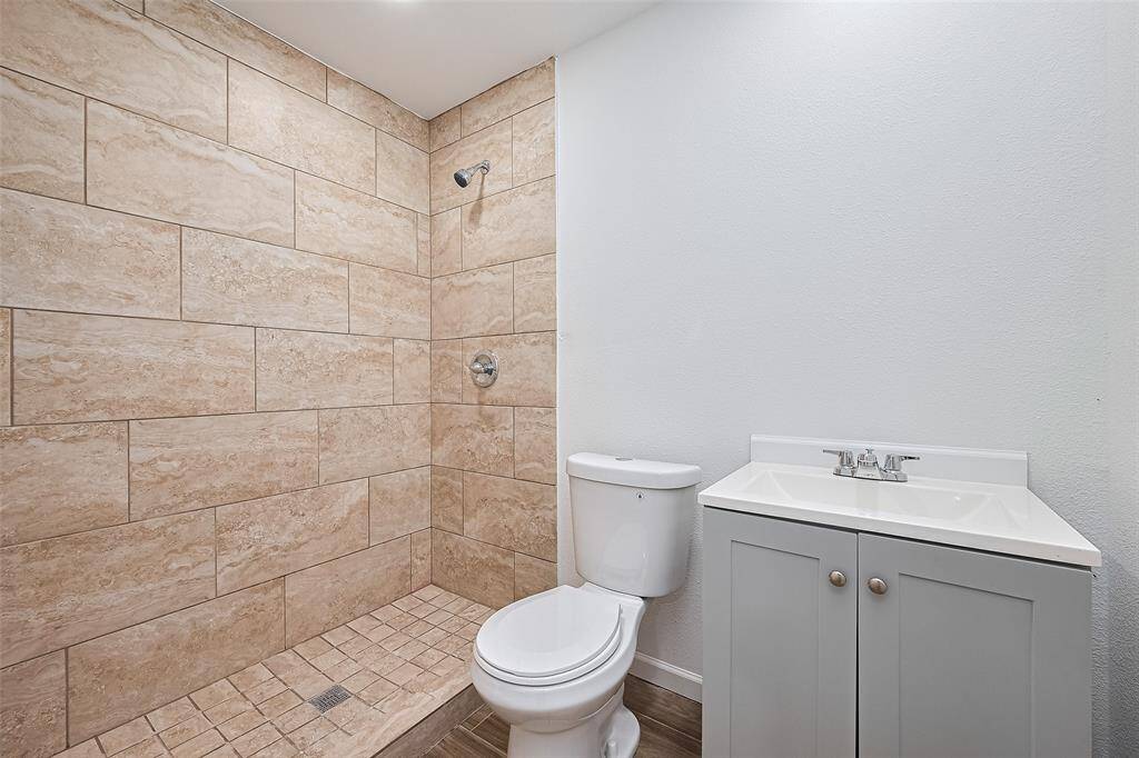 Clean and modern bathroom featuring a walk-in shower with large neutral tiles, a sleek white vanity with brushed nickel hardware, and a simple white toilet.