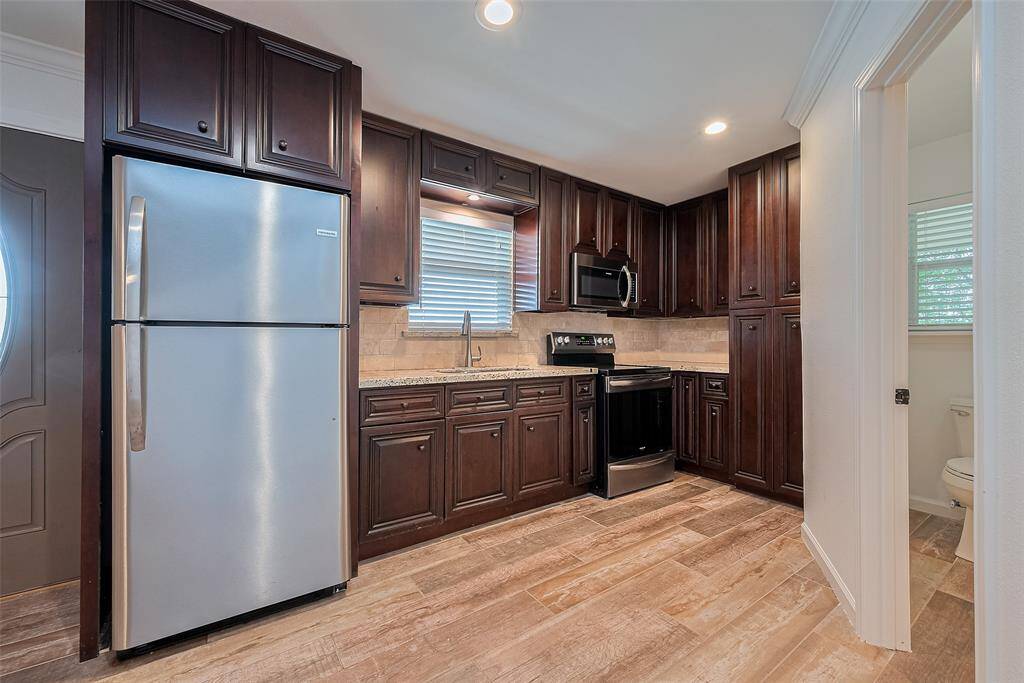 Kitchen featuring rich dark cabinetry, stainless steel appliances, and wood-look tile floors, all illuminated by recessed lighting.