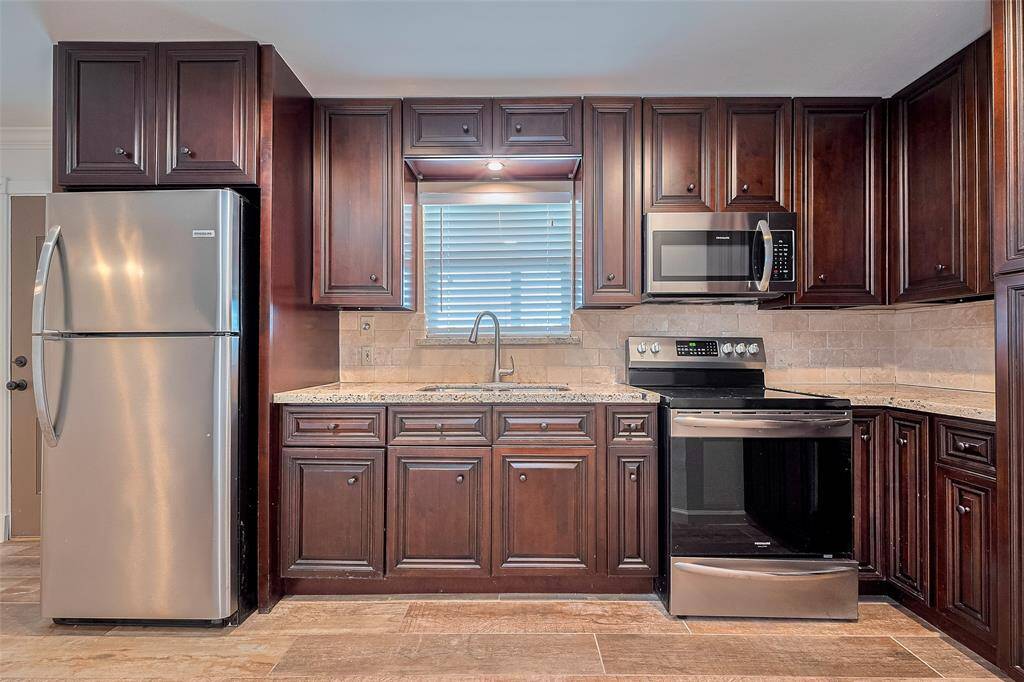 Kitchen featuring rich dark cabinetry, stainless steel appliances, and wood-look tile floors, all illuminated by recessed lighting.