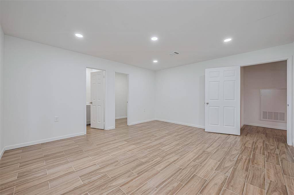 Bright and spacious room with wood-look tile flooring, recessed lighting, and multiple access points—ideal as a bedroom or flexible living space.