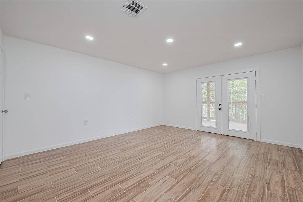 Bright and spacious room with wood-look tile flooring, recessed lighting, and multiple access points—ideal as a bedroom or flexible living space.