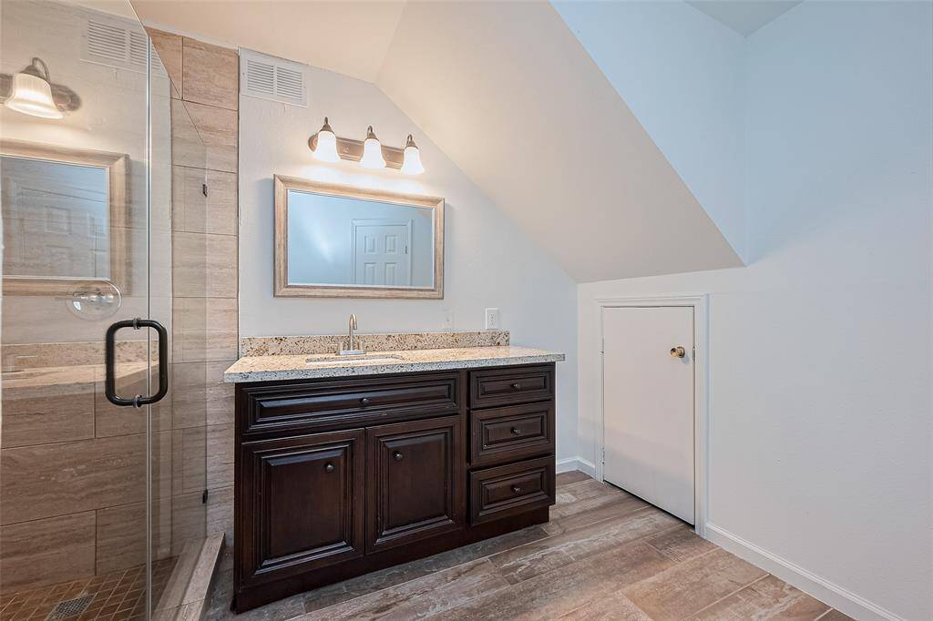 Elegant bathroom featuring a walk-in glass shower with large beige tiles, a rich espresso vanity with granite countertop, a framed mirror, and soft overhead lighting.