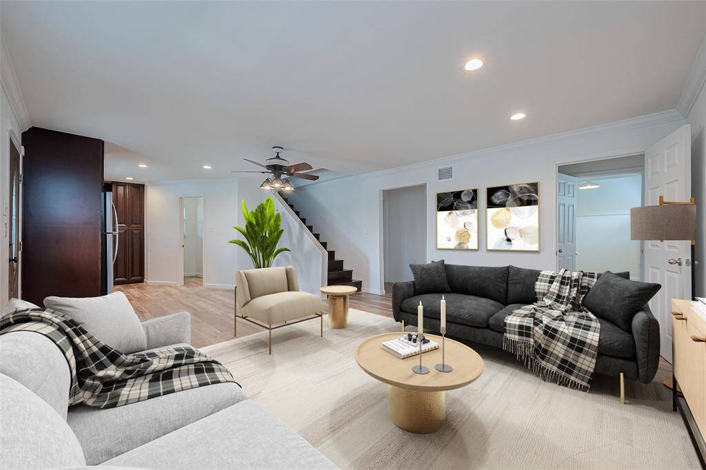 Virtually staged living room with modern furniture, neutral tones, and warm wood flooring. Features include recessed lighting, ceiling fan, and a staircase leading to the upper level, creating a welcoming and spacious atmosphere.