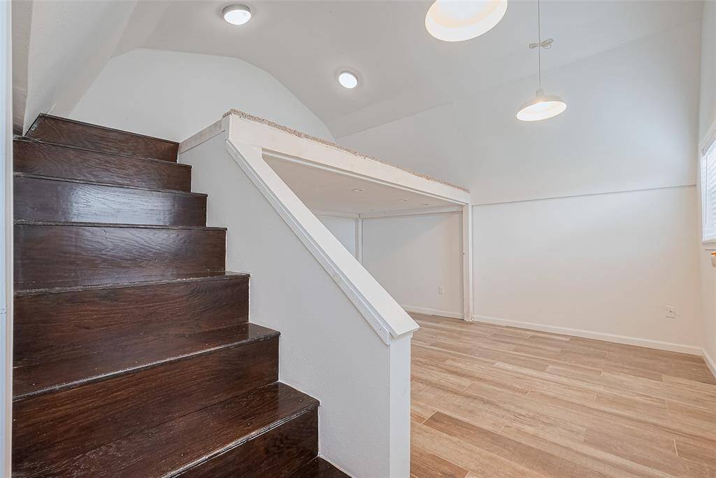 Loft-style upper level with dark wood stairs leading to a cozy open space, featuring vaulted ceilings, pendant lighting, and wood-look tile flooring.