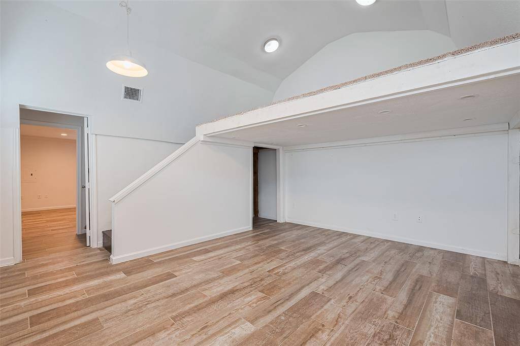 Bright upstairs loft area featuring vaulted ceilings, wood-look tile floors, and a unique raised platform—ideal for a cozy lounge, reading nook, or creative workspace.