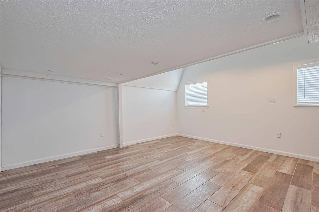 Cozy loft nook featuring wood-look tile flooring, soft natural light from dual windows, and a unique low-ceiling section perfect for a play area, reading space, or extra storage.