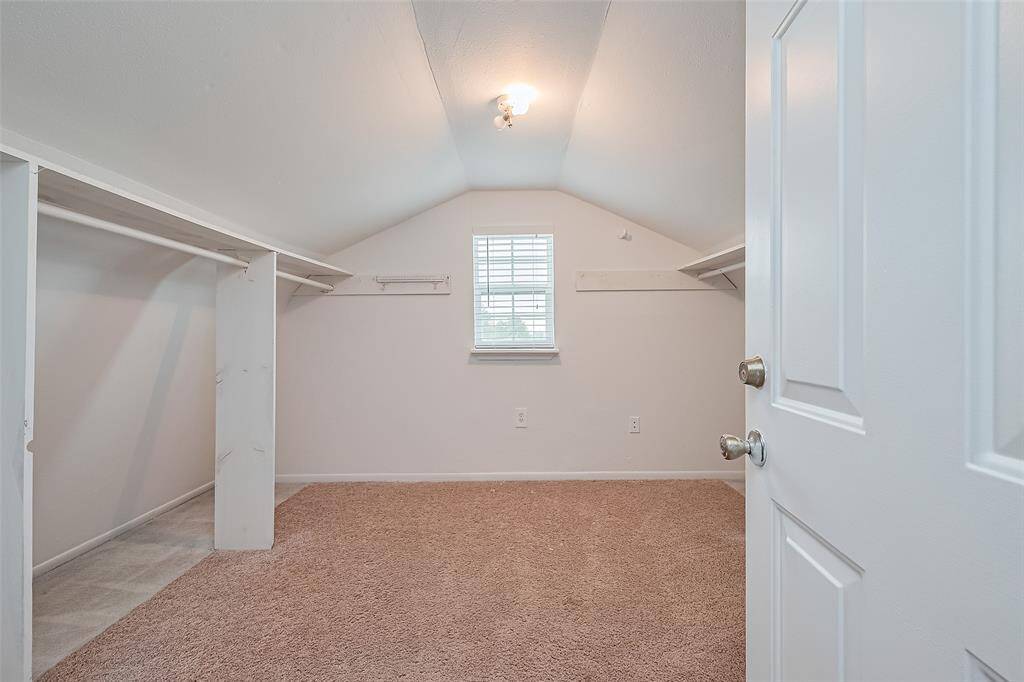 Cozy upstairs walk-in closet with built-in hanging space, neutral carpet, and a charming window that brings in natural light.
