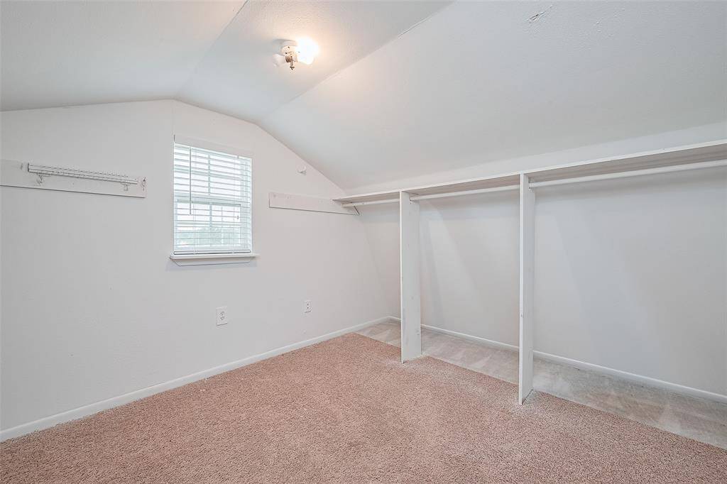 Cozy upstairs walk-in closet with built-in hanging space, neutral carpet, and a charming window that brings in natural light.