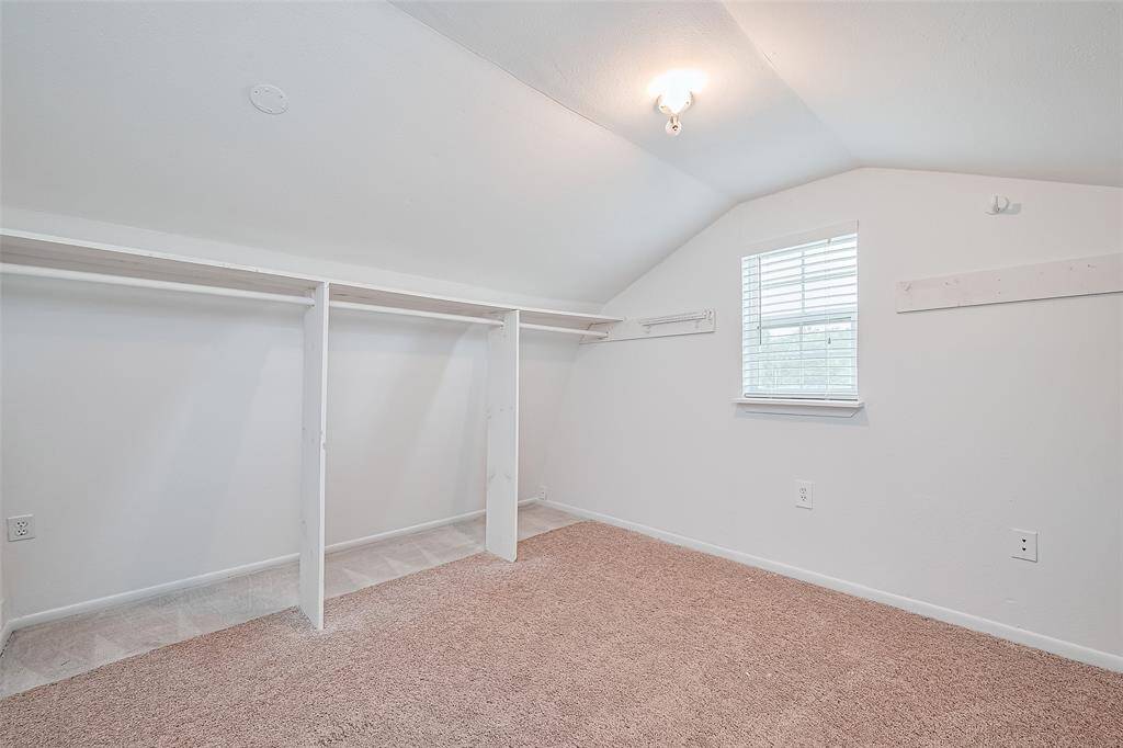 Cozy upstairs walk-in closet with built-in hanging space, neutral carpet, and a charming window that brings in natural light.