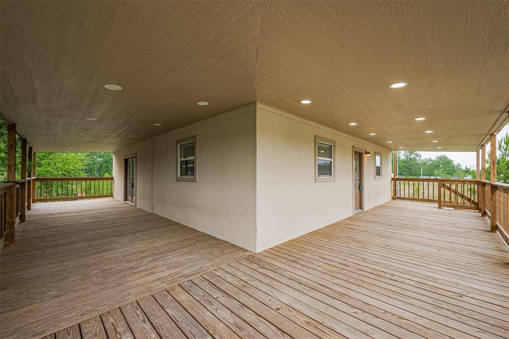 Expansive wraparound wooden porch with recessed lighting, offering dual access points and peaceful views—perfect for relaxing or entertaining.