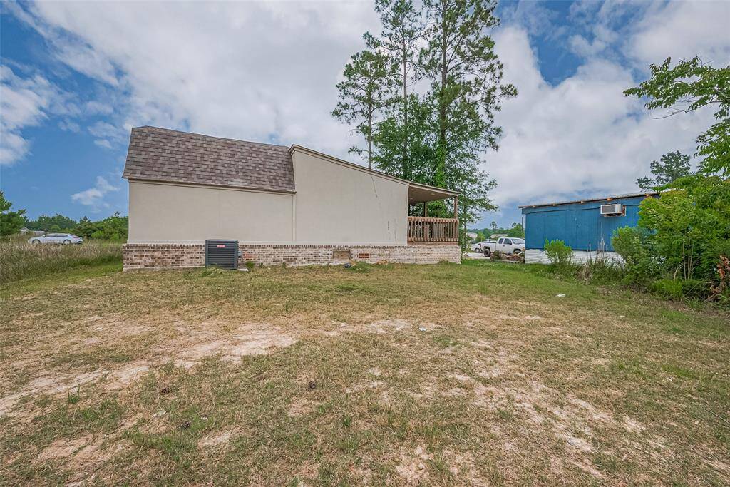 Side view of the home highlighting the expansive yard, partial brick exterior, and covered wraparound porch—offering a blend of privacy and outdoor versatility.