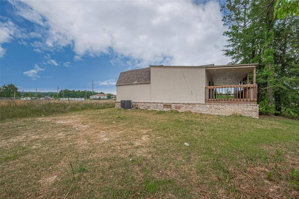 Side yard view showcasing the full depth of the lot and the elevated brick foundation of the home, along with a spacious covered porch perfect for relaxing outdoors.
