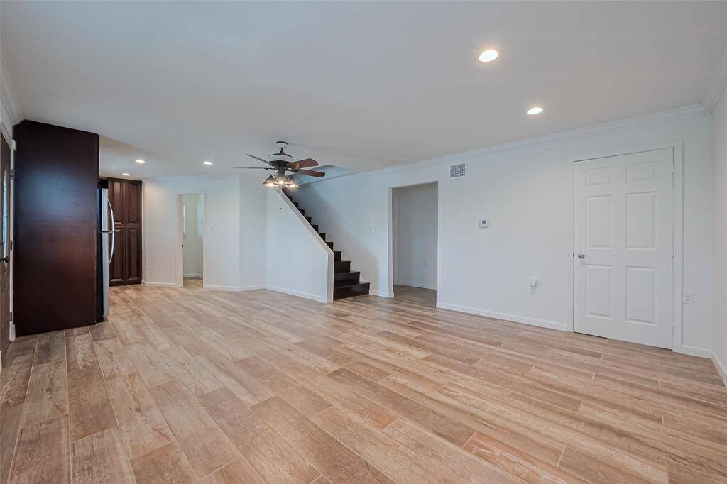 Open-concept living space with rich wood-look tile floors, neutral walls, and a ceiling fan, perfect for flexible furniture arrangements.