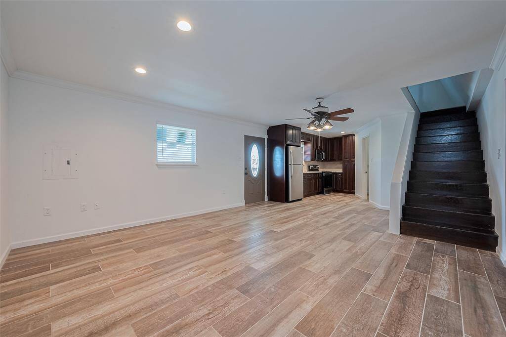 Open-concept living area with wood-look tile flooring, recessed lighting, and a modern kitchen featuring dark cabinetry and stainless steel appliances.