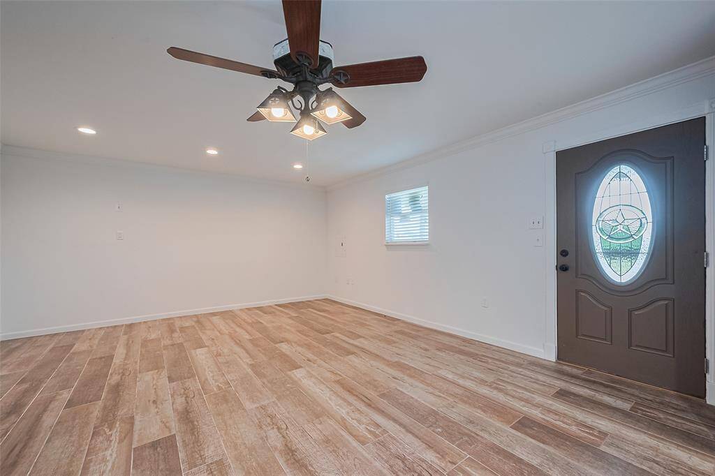 Open-concept living space with rich wood-look tile floors, neutral walls, and a ceiling fan, perfect for flexible furniture arrangements.