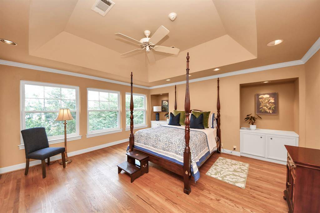 This spacious primary suite offers a beautiful coffered ceiling, glowing natural light, and charming built-in nooks with cabinets flanking the bed—ideal for books, décor, or nighttime essentials.