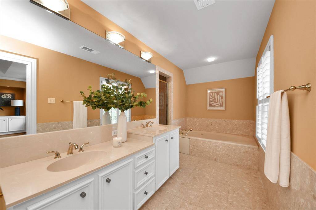Enjoy a spa-inspired primary bath with dual vanities, a relaxing jetted tub, and a generous walk-in shower finished with beautifully crafted custom tile.