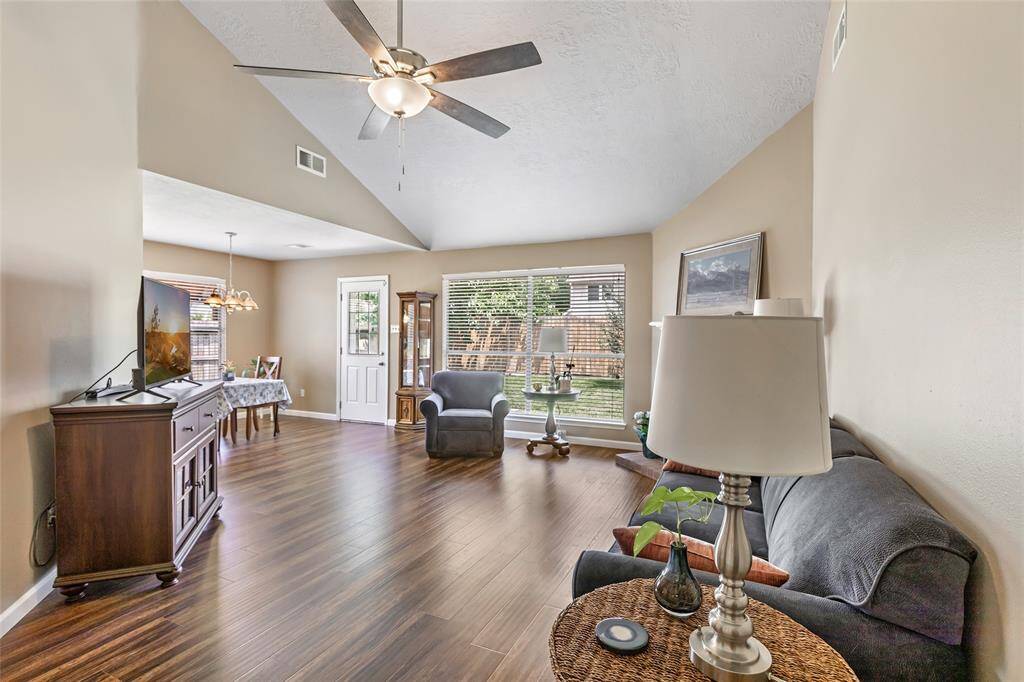 This inviting living area features high ceilings, warm laminate wood flooring, and abundant natural light from large windows. An open layout seamlessly connects to a cozy dining space, creating a perfect setting for relaxation and entertainment.