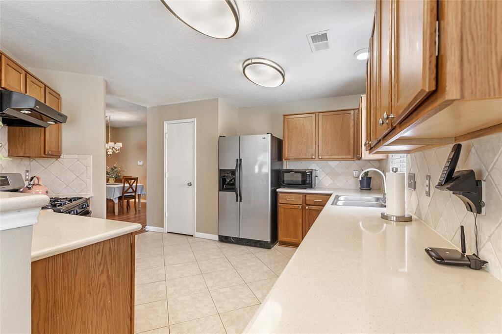 This kitchen features modern stainless and black appliances, ample wooden cabinetry, and a spacious Silestone countertop with Travertine backsplash.