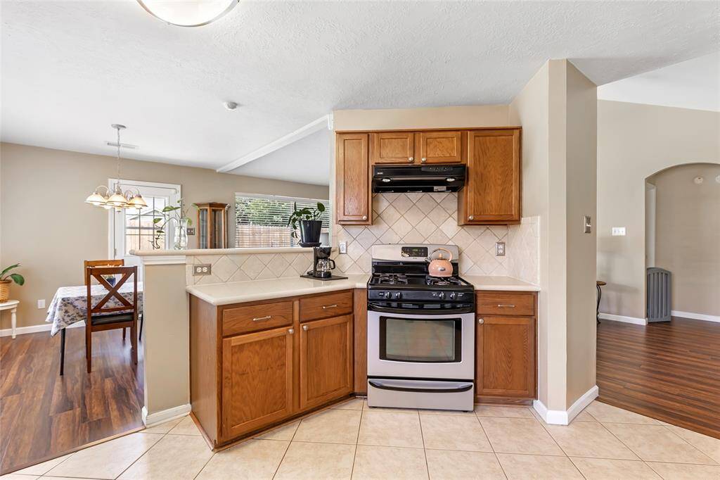 This kitchen features a cozy yet spacious layout with stainless steel appliances and wooden cabinetry. It opens to a bright dining area with wood flooring and ample natural light. The space has a warm, inviting atmosphere, perfect for family gatherings.