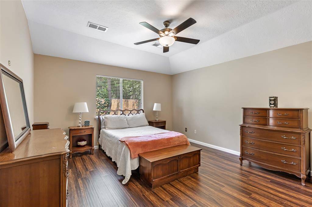 This spacious primary bedroom features warm wood flooring, neutral walls, and a ceiling fan. Natural light filters in through a window that overlooks the backyard, enhancing the room's warmth.