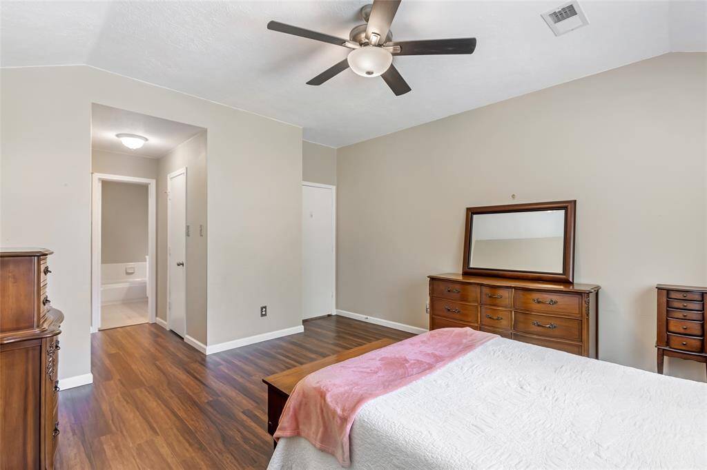 Spacious primary bedroom with laminate wood floors, neutral walls, and a ceiling fan. Includes an ensuite bathroom, closet and offers a functional layout.