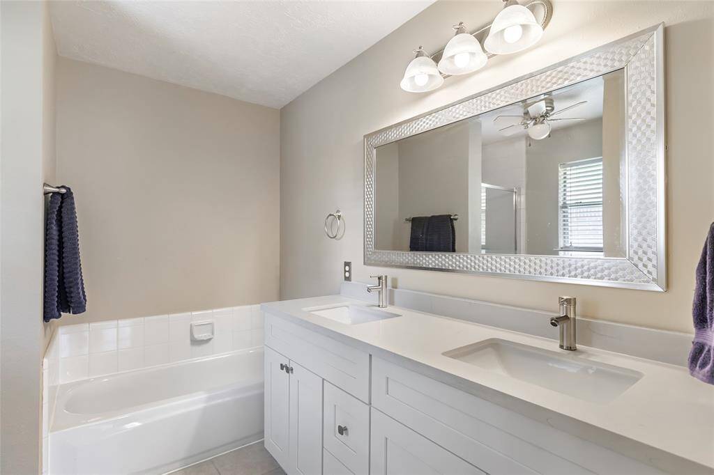 The primary bathroom features a modern design with an updated double vanity, sleek faucets, and ample storage. It includes a large, framed mirror and a clean, white bathtub, creating a bright and inviting space.