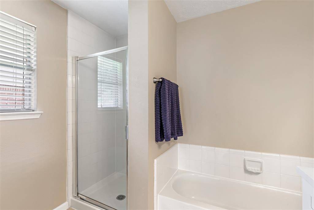 Another view of the primary bathroom features a clean and modern design with a glass-enclosed shower, a bathtub with white tile surround, and a neutral color palette. A window provides natural light, and a towel rack is conveniently placed near the tub.